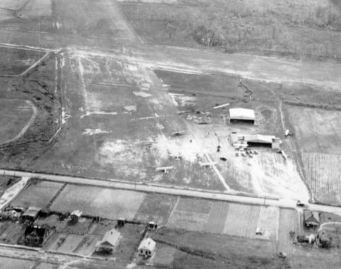 Black and white aerial photo of the airport with two hangars and several small planes