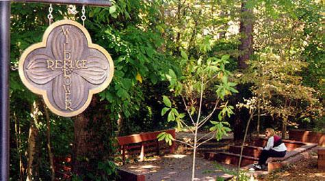 Four leafed clover shaped sign for the Wildflower Refuge, near small seating area overlooking the woods