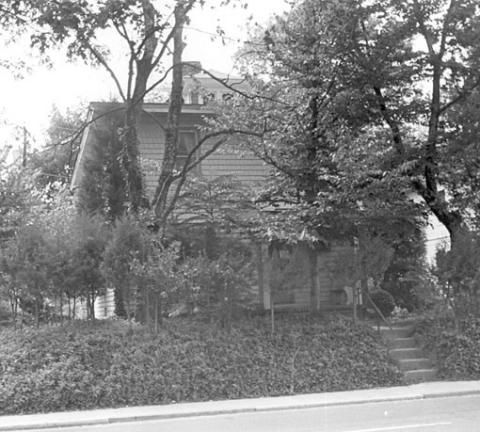 Black and white photo of the Holmes house as seen from the road covered by trees