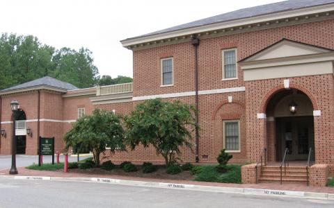 Two story brick building with covered arch entry and two tree on the side.