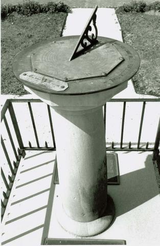 Black and white photo of the sundial atop a plinth and surrounded by a low fence