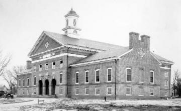 Black and white photo of two story brick building with three arches at the front entrance