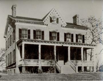 Black and white photo of two story colonial house with full covered porch on the front