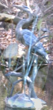 Metal statue of the profile of a blue heron standing on a branch in a pond