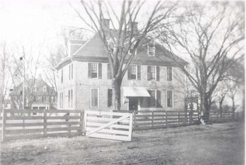Black and white photo of the Brafferton, circa 1907, with a wood picket fence and awning over the front door.