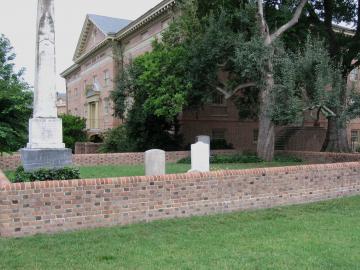 Brick fenced cemetery with several stone tombstones and Blow Hall in the distance