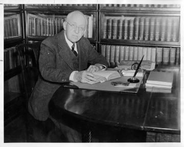 Black and white photo of Earl Gregg Swem seated at a desk in front of a wall of bookcases