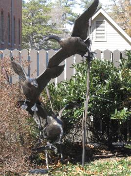 Metal statue of three canadian geese in flight and flying vertically above one another