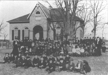 Small brick building in background with a large group of students sitting outside
