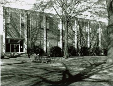 Black and white photo of two story brick building with column of windows